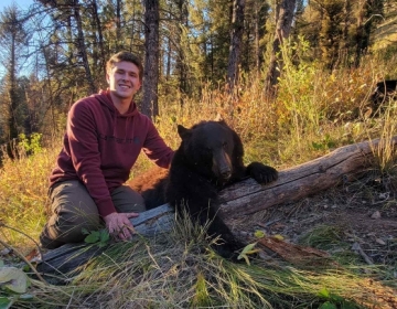 A non resident fall black bear hunter poses with his color phase black bear in the mountains of Wyoming.